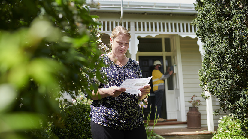 Woman standing out the front of her home looking at an electricity bill