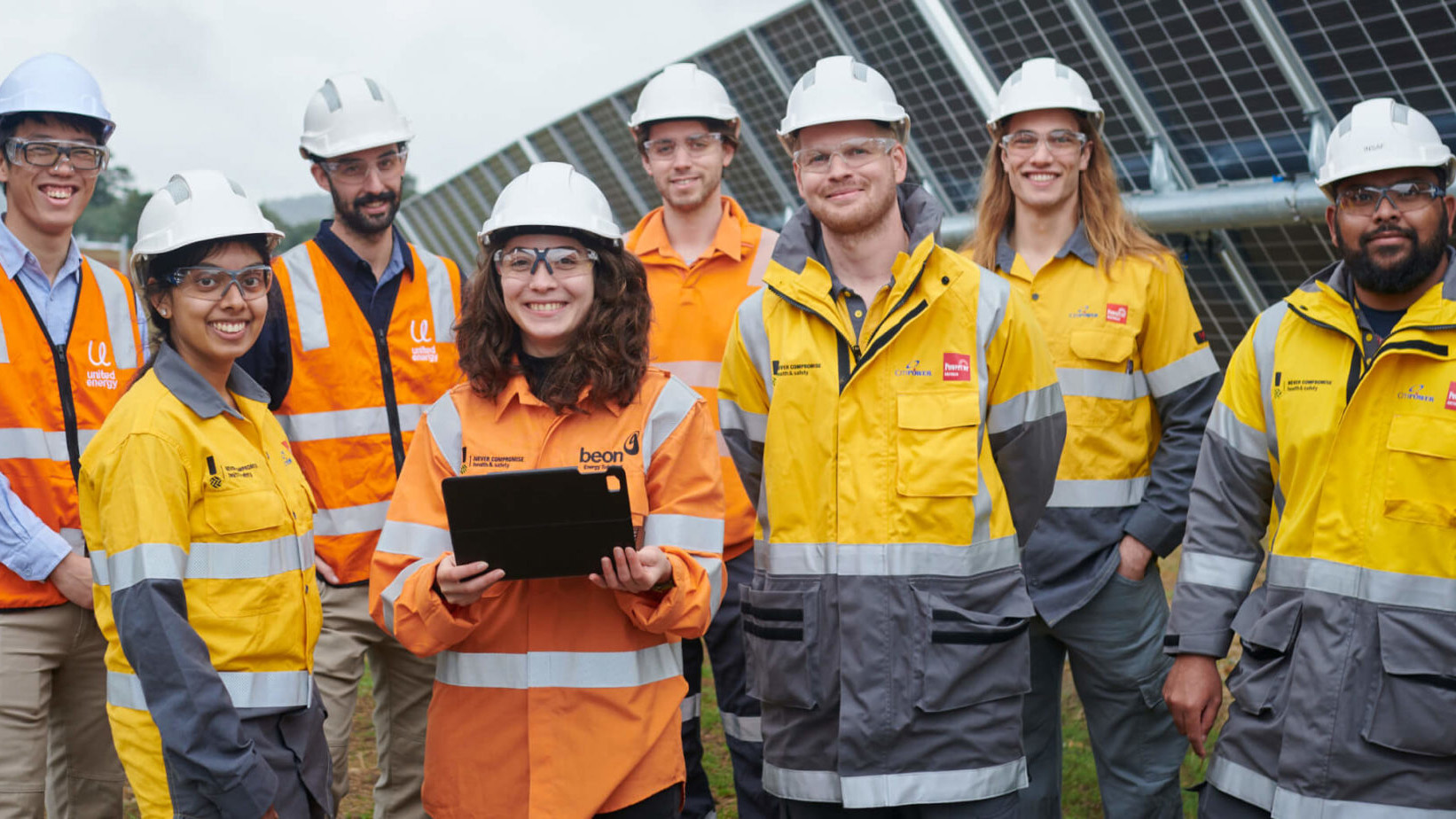 Graduates in hi-vis standing and smiling with solar panel in the background